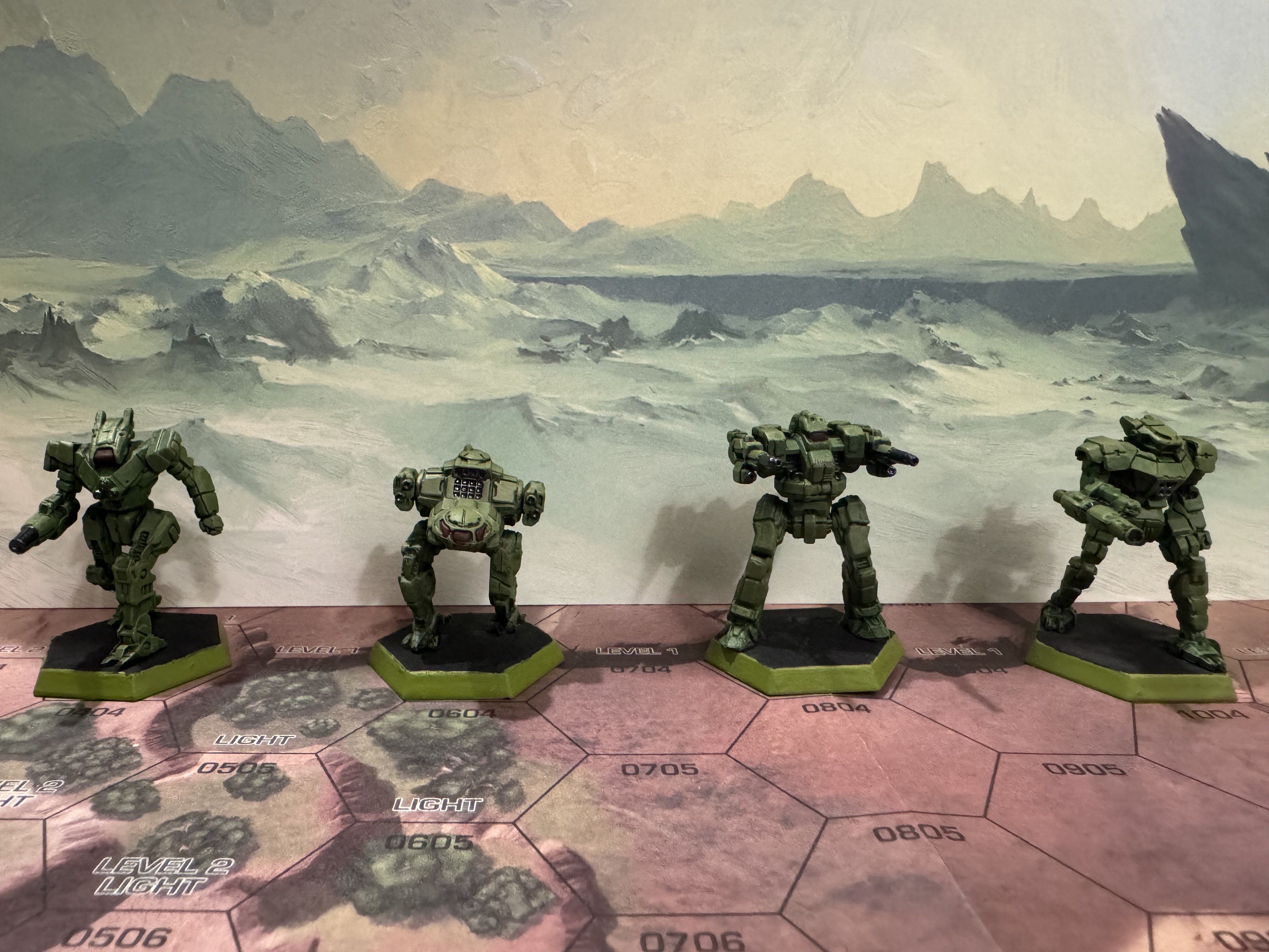 The Inner Sphere Assault Lance painted in military green/brown with red tinted windows and metal weaponry. They are displayed on a hex map with an ice world backdrop